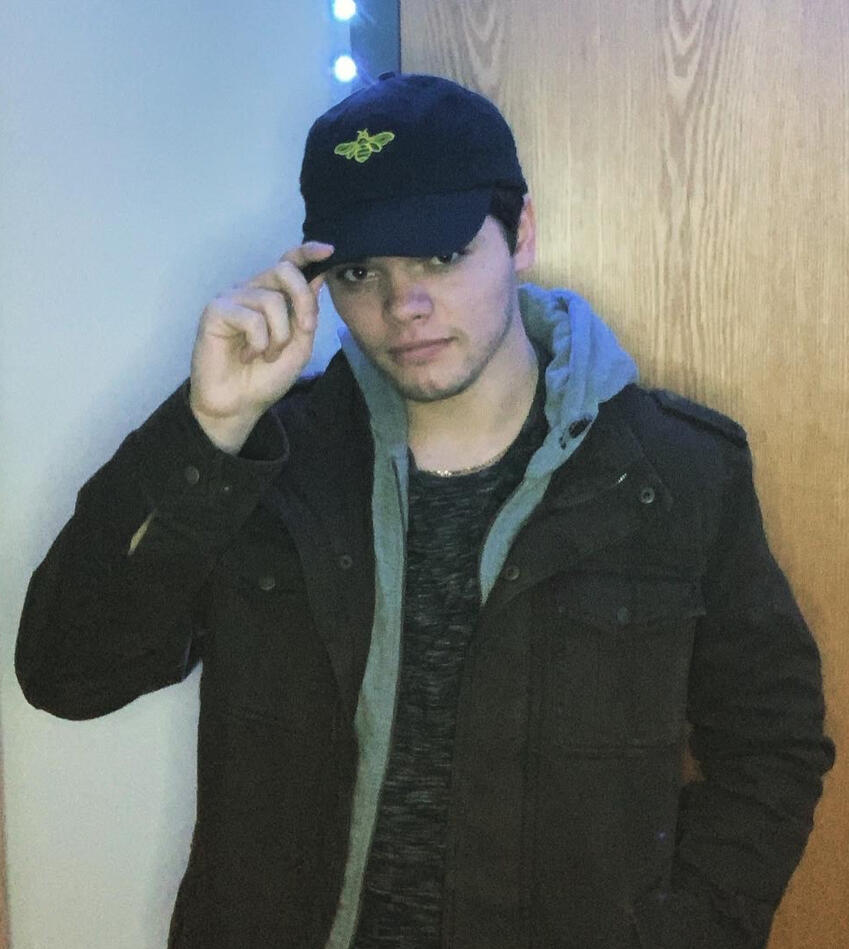 Treverse standing in a doorway with a jacket and a bee-themed hat.